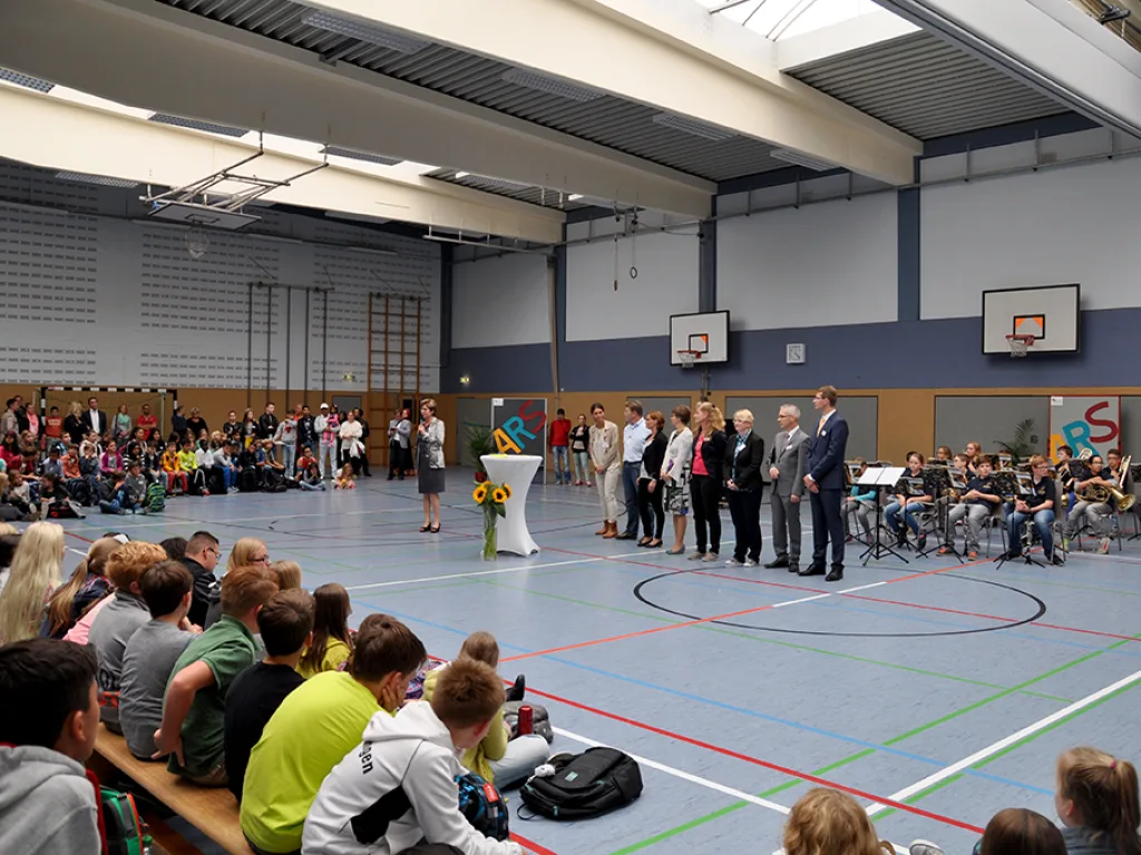 Mehrere Erwachsene stehen bei der Begrüßung vorn in der Halle.